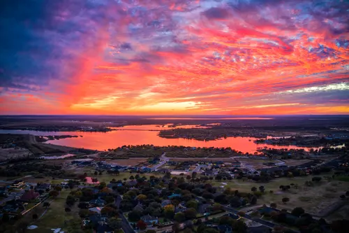 Aerial view of a reservoir and neighborhoods beneath a vivid red sunset